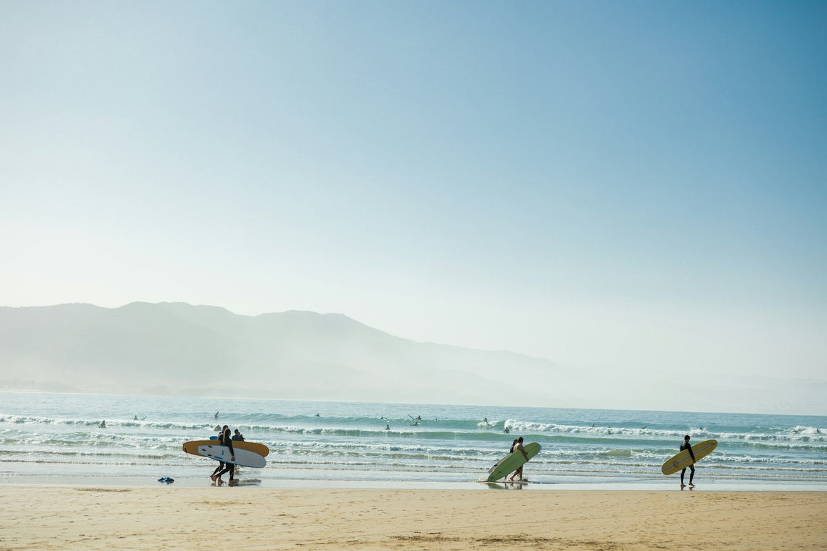 A group of people carrying surfboards on a beach in Imsouane, Morocco