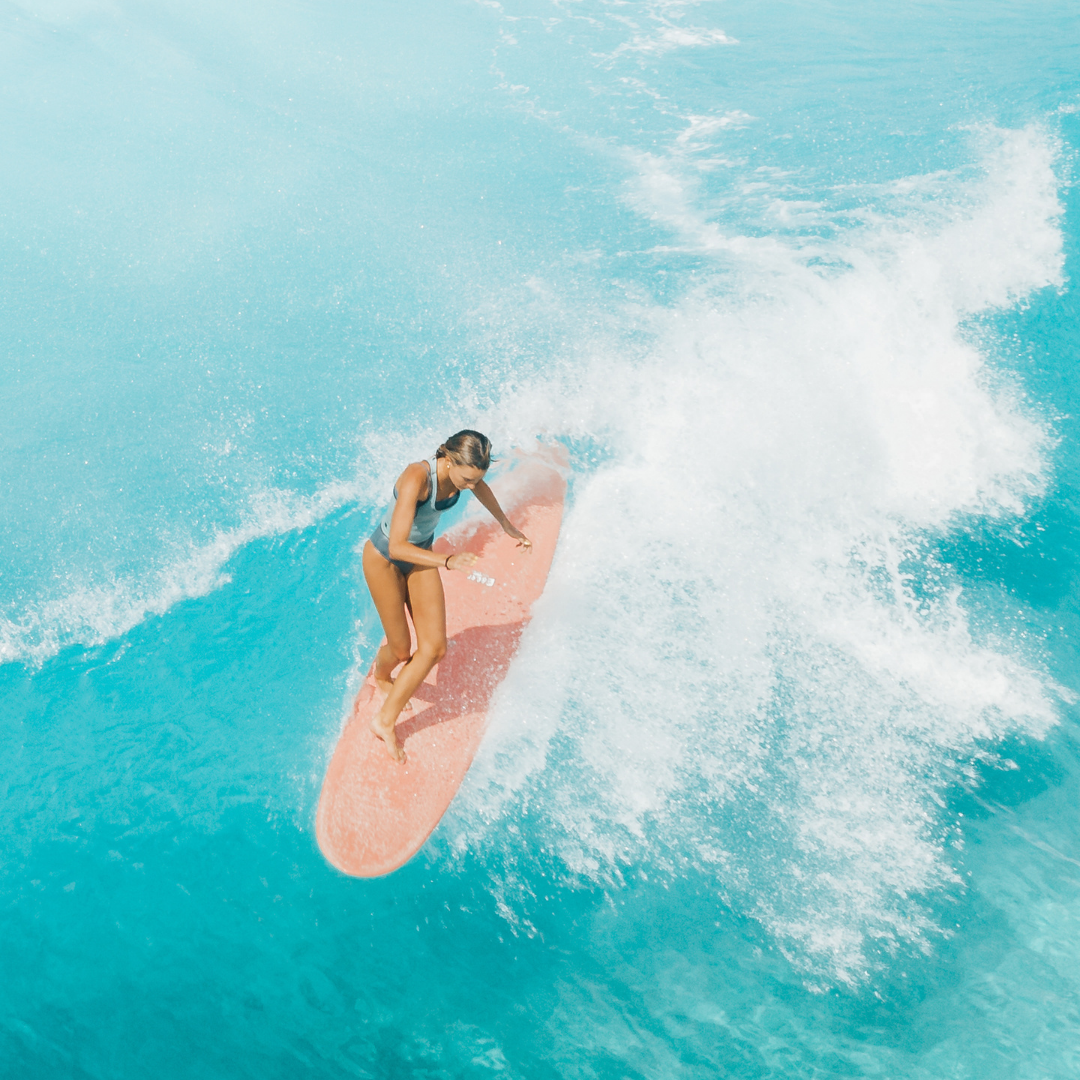 Surfer riding a pink longboard through turquoise whitewater, seen from above