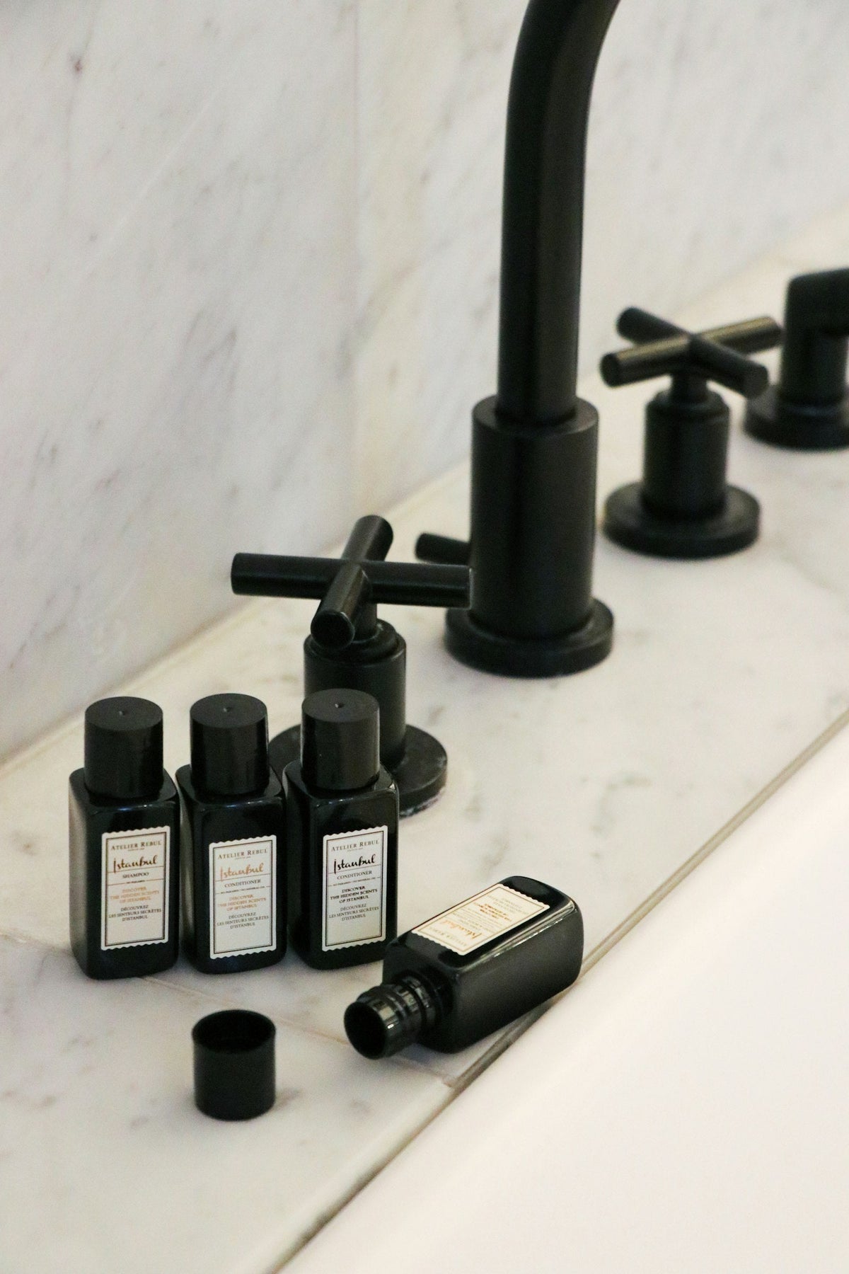 Lavabo de salle de bain d’hôtel avec des flacons de savon à côté d’un robinet noir