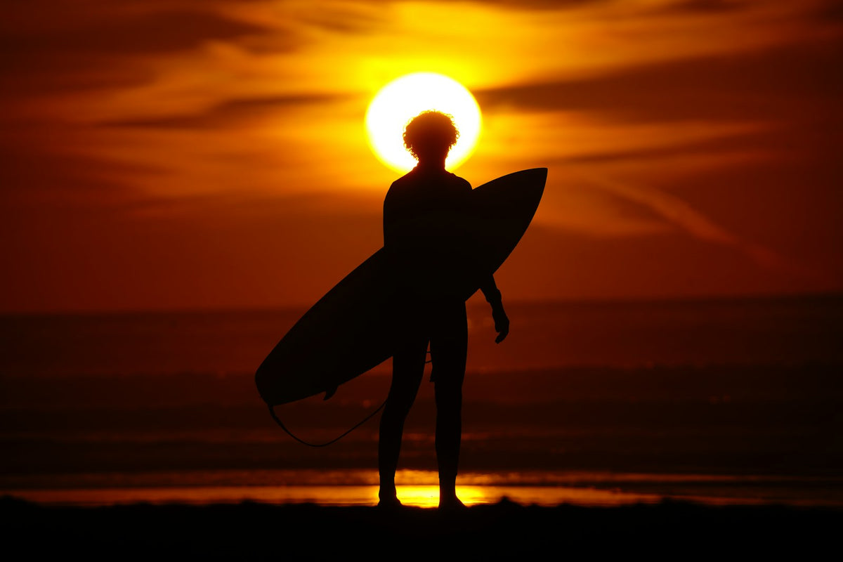Silhouet van een eenzame surfer met een surfplank bij zonsondergang in Taghazout, Marokko