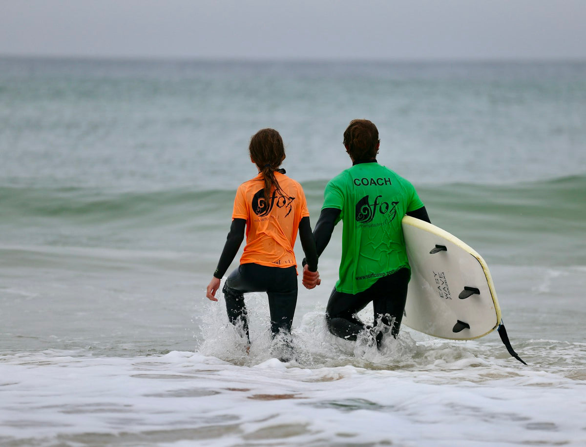 Surfcoach begeleidt een beginner met een surfplank de zee in bij Peniche, Portugal