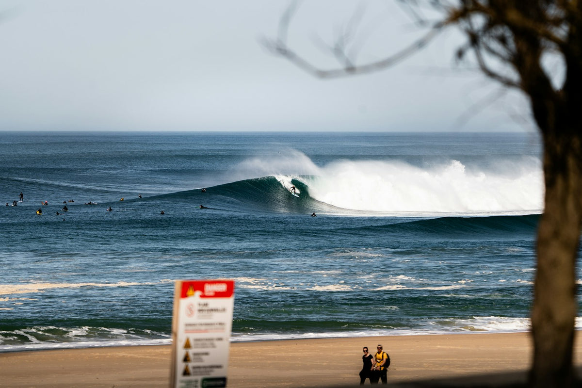 Surfer riding a powerful barrel at La Nord in Hossegor, France, with surfers waiting in the line-up