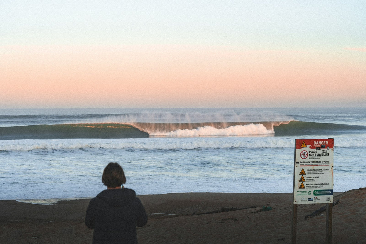 Person watching Atlantic waves break under a pastel sunset sky in Hossegor, France