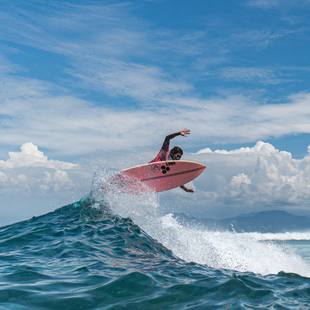Surfer on a pink surfboard launching off the lip of a blue wave